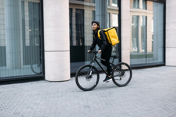 Smiling courier girl riding a bicycle wearing delivery thermal backpack looking for a customer...
