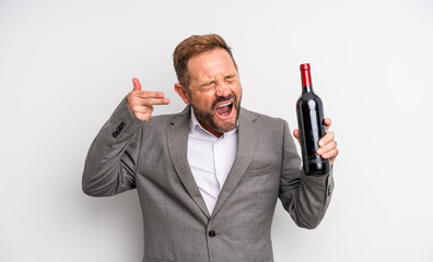 middle age handsome man looking unhappy and stressed, suicide gesture making gun sign. wine bottle...