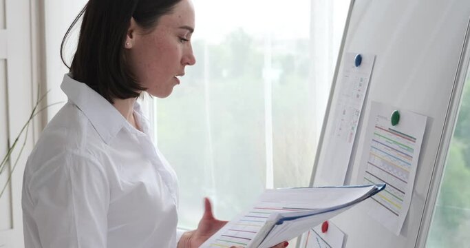 Businesswoman analyzing paperwork and filling form on whiteboard at office