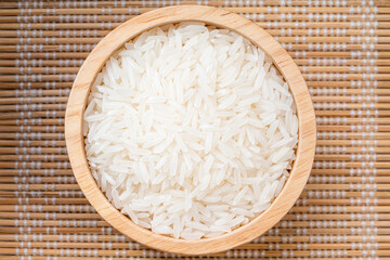 Jasmine rice  in wooden bowl on bamboo mat background.