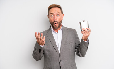 middle age handsome man amazed, shocked and astonished with an unbelievable surprise. alcohol flask...
