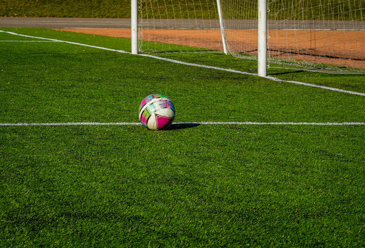 Photo of the ball on the green lawn of the football field near the gate on the street