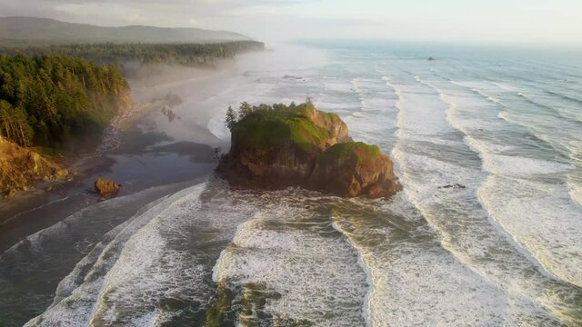 Pacific waves and huge stones on the shore in sunset light, fog on the beach. Flying over Ruby beach, Oregon, United States. Aerial view of Pacific coast in USA