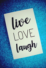 Live Love Laugh text on paper card top view on blue bokeh background