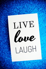 Live Love Laugh text on paper card top view on blue bokeh background
