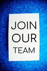 Join our team text on paper card top view on blue bokeh background