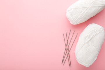 White wool clews and metal needles on light pink table background. Pastel color. Closeup. Knit clothes or other things. Empty place for text. Top down view.