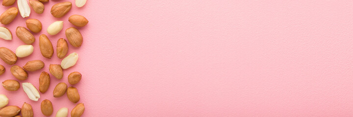 Brown almond nuts on light pink table background. Pastel color. Closeup. Food wide banner. Empty place for text. Top down view.