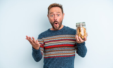 middle age handsome man amazed, shocked and astonished with an unbelievable surprise. cookies bottle