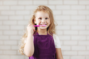 A little charming girl is brushing her teeth with a bright pink toothbrush. Oral care, hygiene, prevention. Space for text