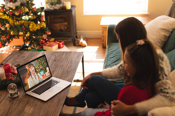 Caucasian mother and daughter in santa hat on christmas laptop video call with friend