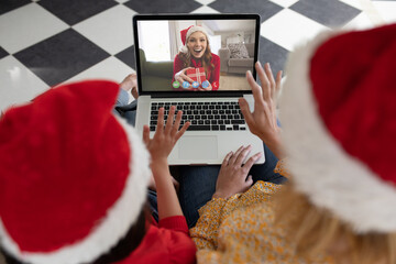 Caucasian mother and child in santa hat on christmas laptop video call with friend