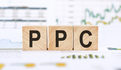 Word PPC - pay per click, made with wood building blocks on background from financial graphs and charts.