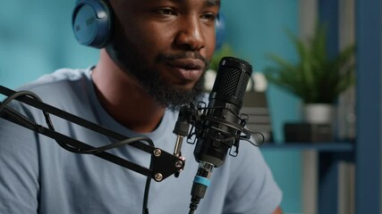 Close up of vlogger using microphone for conversation with subscribers while wearing headphones. Social media influencer recording online podcast and talking to audience with gear.