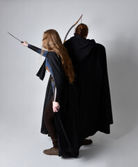 Full length  portrait of red haired  couple, man and woman wearing medieval viking inspired fantasy costumes, standing fighting pose holding  archery bow and arrow and long sword weapons, isolated on 