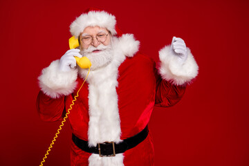 Photo of pretty handsome man pensioner dressed santa claus costume talking retro phone empty space smiling isolated red color background
