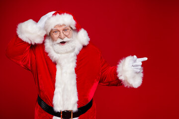 Photo of handsome impressed man pensioner dressed santa claus costume pointing finger empty space isolated red color background