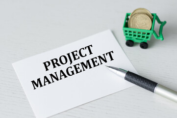 Business card with text Project Management lying on a table next to a pen and coins, concept
