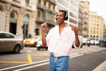 Fototapeta premium Cheerful guy with the headphones. Young african man listening the music outdoors.