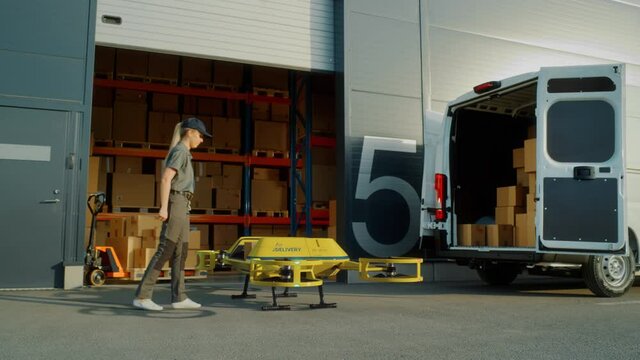 Storage Facility Female Worker Loads Up Autonomous Flying Delivery Drone with a Parcel, Confirms Destination. Futuristic Parcel Drone Takes Off on Flight from Warehouse to Client Waiting for Package