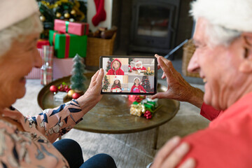 Happy caucasian senior couple making tablet christmas video call with four smiling granddaughters