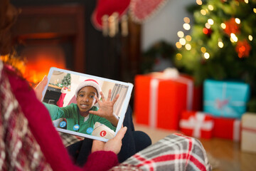 Caucasian woman on christmas tablet video call with african american boy