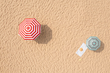 Fototapeta na wymiar Striped beach umbrellas, towel, hat and flip flops on sandy coast, aerial view
