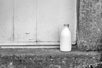 A pint glass bottle of milk with a silver top delivered to a house with a stone step and wooden...