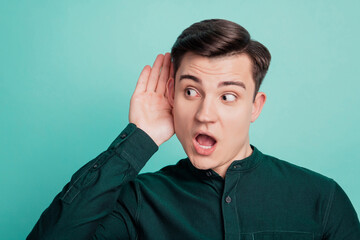 Portrait of surprised guy hand ear eavesdropping open mouth look empty space on turquoise background
