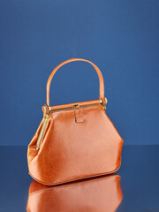 Fashionable handbag made of yellow-red leather, standing on a mirror surface, on a rich blue background with reflection. Copy space. Vertical image.
