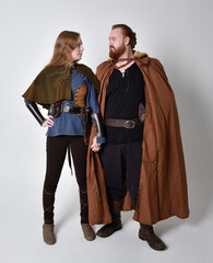 Full length  portrait of red haired  couple, man and woman wearing medieval viking inspired fantasy costumes, standing pose, isolated on white  studio background. 