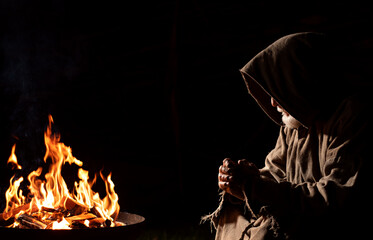 Old medieval man prays by the campfire