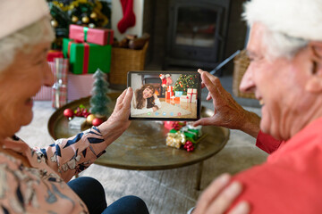 Caucasian grandparents in santa hats on christmas video call on tablet with granddaughter