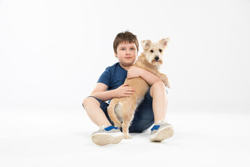 A young boy sits on a white background and in his hands he holds his beloved dog.