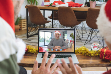 Obraz na płótnie Canvas Caucasian couple in santa hat on christmas video call on laptop with senior male friend
