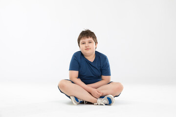 A young boy sits cross-legged on a white background.