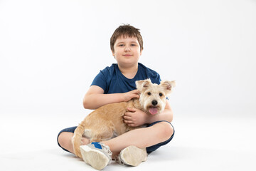 A young boy sits on a white background and in his hands he holds his beloved dog.