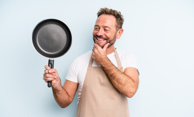 middle age handsome man smiling with a happy, confident expression with hand on chin. frying pan...