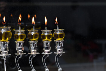 Hanukkah candles made of olive oil are lit in a silver menorah against the backdrop of the darkness of the night
