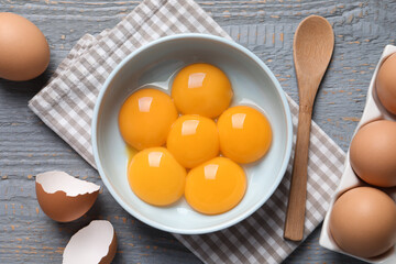 Chicken eggs and bowl with raw yolks on grey wooden table, flat lay - obrazy, fototapety, plakaty