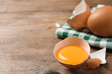 Cracked raw chicken egg with yolk on wooden table, closeup. Space for text