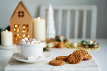 Cozy home Christmas atmosphere in living room, festive holiday home. Homemade chip cookies and cup of hot chocolate on table, chair near grey wall. Cozy xmas evening. Selective focus