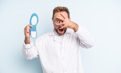 middle age handsome man looking shocked, scared or terrified, covering face with hand.  podiatrist...