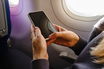 Woman takes pictures on the phone from the airplane window. Hand with a telephone near the porthole. Airplane wing, scenic view. Beautiful cloud, blue sky. Travel by plane, adventure. Air Transport