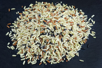 Heap of rice mixed from different varieties on a black board. a mixture of raw parboiled and wild rice. Rice berry, Black jasmine, Red jasmine, Brown rice and Jib brown.
