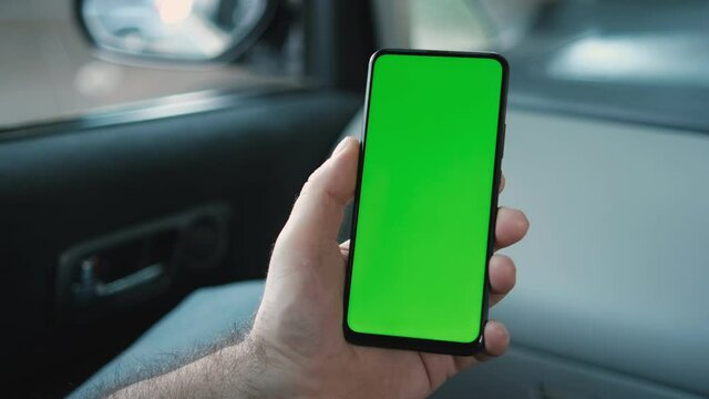 Handheld Camera: Back View of Man in car Holding Chroma Key Green Screen Smartphone Watching Content Touching or Swiping.