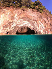 Underwater split photo of small white rock cave with crystal clear emerald sea and chapel of Agios Nikolaos built inside the cave, Desimi beach, Lefkada island, Ionian, Greece