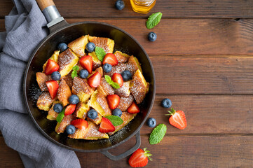 Kaiserschmarrn - traditional austrian pancake dessert with fresh berries and powdered sugar on a dark wooden background. Sweet breakfast. Copy space.