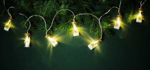 Christmas banner with fir branches and Christmas garland on a green background, top view. Festive new year background.