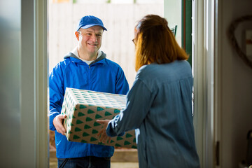  Woman at home standing in doorway, receiving parcels for Christmas gifts. Delivery man bringing...